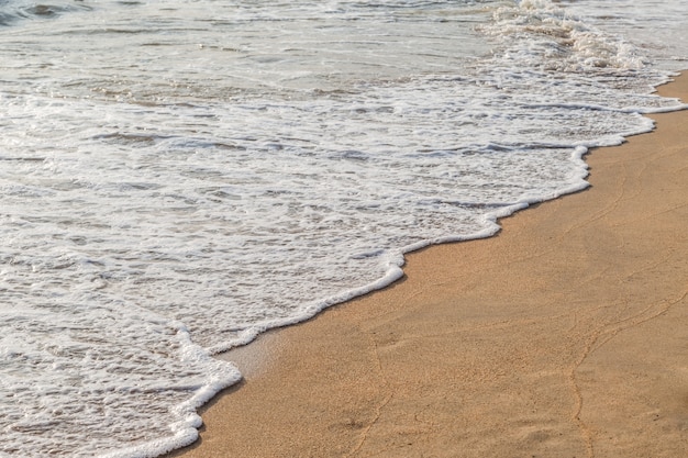 Ola de agua blanca del mar en el fondo de la playa de arena