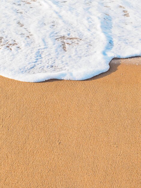 Ola de espuma de mar de tiro vertical en un espacio de copia de playa de arena