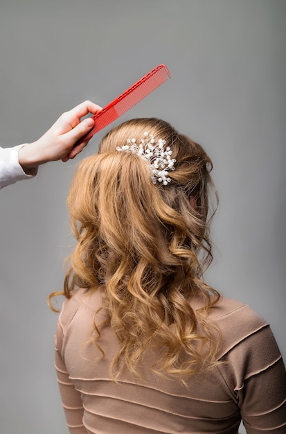 Foto ola rizos peinado. peluquero que hace el peinado a la mujer del pelo rubio con el pelo largo usando el peine en fondo gris.