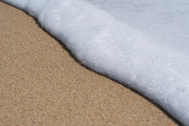 Ola suave del mar en la playa de arena blanca con espuma limpia en un día soleado. Concepto de naturaleza