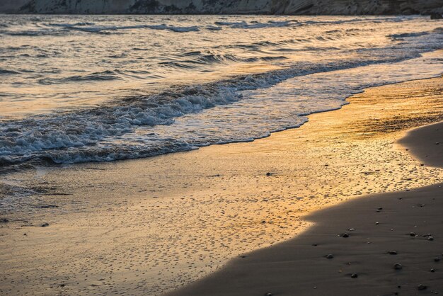 Las olas se acercan a la playa de arena durante la puesta de sol