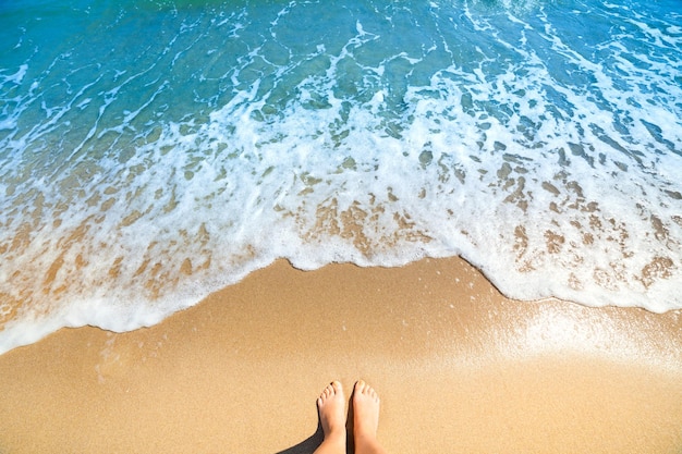 Olas de espuma de mar y pies descalzos en una playa de arena Vacaciones relajarse fondo de verano
