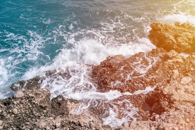 Olas espumosas de agua de mar azul clara golpean contra la costa rocosa de la llamarada del océano