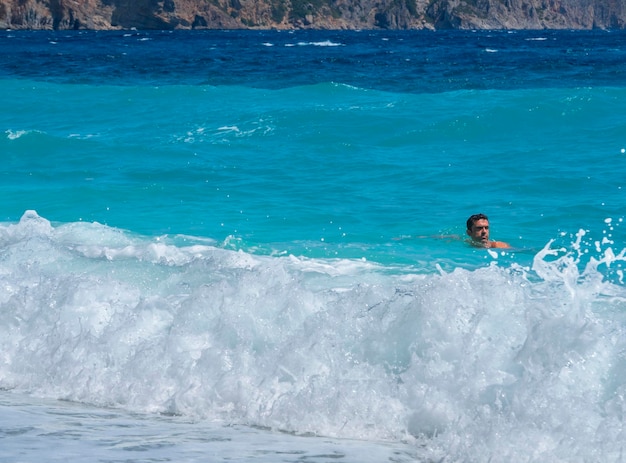 Olas espumosas y turistas bañándose en la playa en el Mar Egeo en Grecia