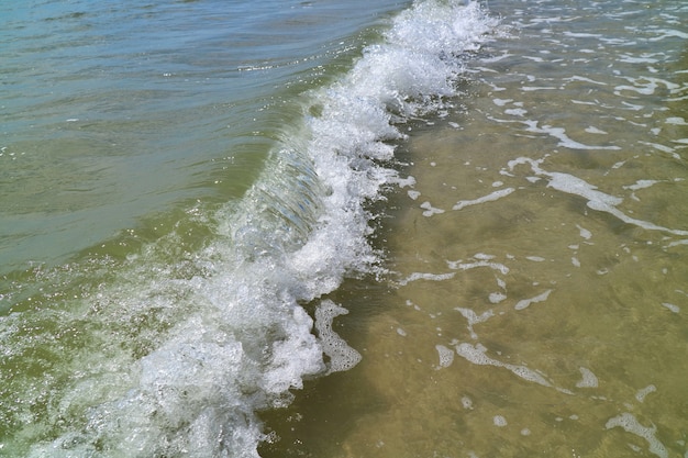 Las olas golpean en la playa con arena y reflejo de la luz solar en la mañana de verano.