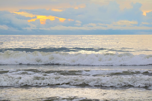 Las olas golpean en la playa con cielo anaranjado y nubes blancas en el mes.