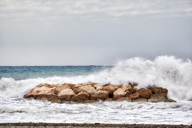 Olas del mar rompiendo fuertemente contra un rompeolas cerca de la orilla de la playa en un día de mar embravecido y mal tiempo