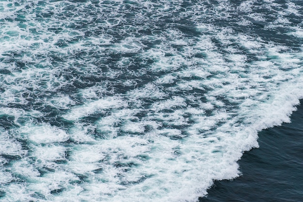 Olas oceánicas blancas que se estrellan sobre rocas costeras del mar en verano.