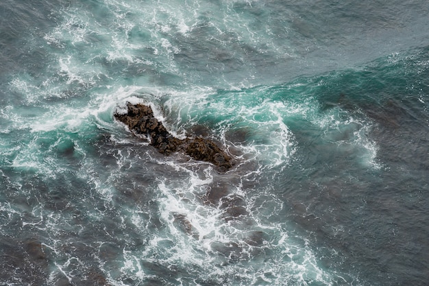 Olas oceánicas blancas que se estrellan sobre rocas costeras del mar en verano.