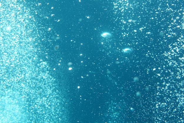 Olas del océano azul bajo el agua con burbujas. Rayos de luz brillando a través. Ideal para fondos.