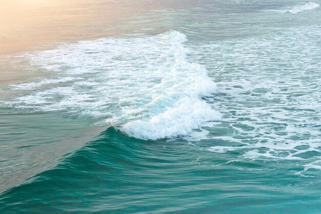 Olas del océano turquesa verde vespertino con espuma en la costa