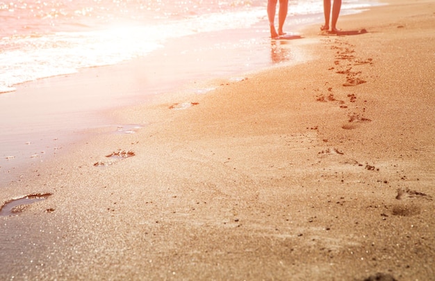 Olas de playa y huellas de mujeres al atardecer con destellos de sol