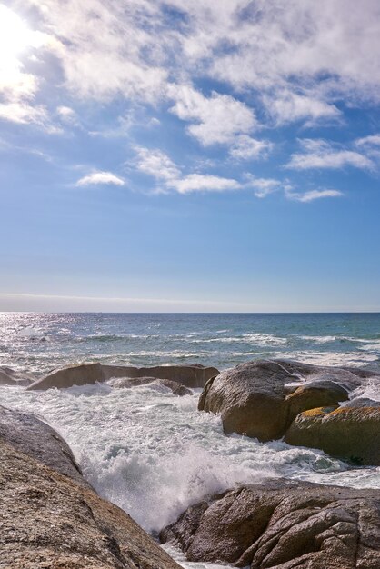 Olas rompiendo contra las rocas en el océano bajo un cielo azul nublado con espacio de copia Paisaje escénico de rocas o grandes piedras en el mar en un popular lugar de verano en Ciudad del Cabo Sudáfrica