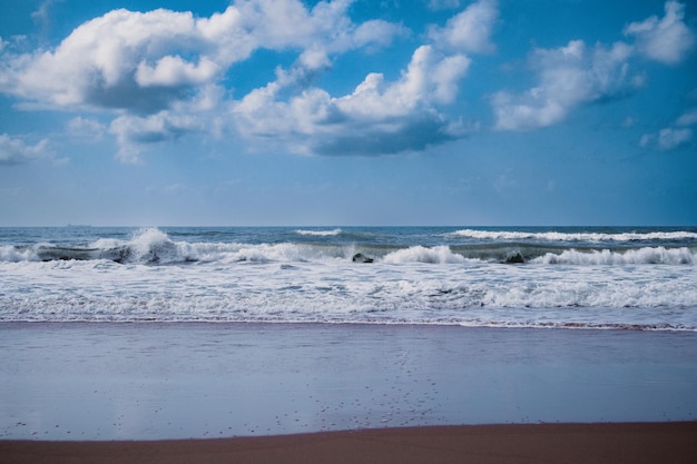 Olas rompiendo en la playa con cielo azul y nubes