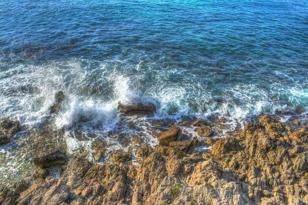 Olas rompiendo sobre rocas marrones en Cerdeña Italia