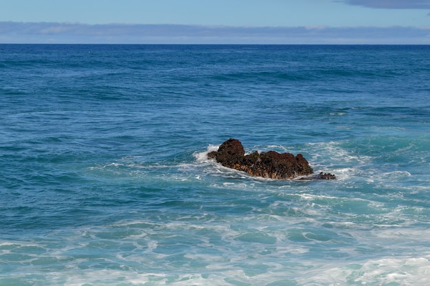 Foto olas sobre una roca negra en medio del mar