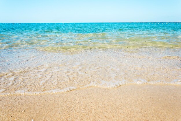Olas suaves con espuma de océano azul en la playa de arena