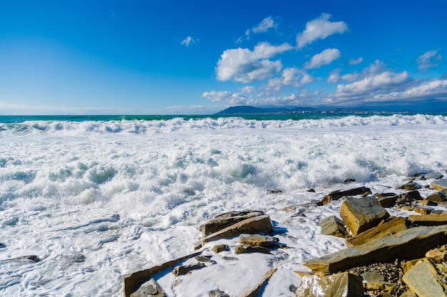 Olas de tormenta en espuma blanca se rompen en la playa sembrada de fragmentos de rocas areniscas amarillentas