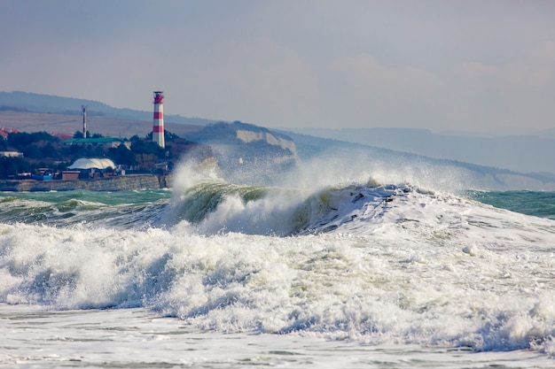 Olas de tormenta hermosas y peligrosas por el faro de Gelendzhik. Resort Gelendzhik, Cáucaso, escarpada costa rocosa.