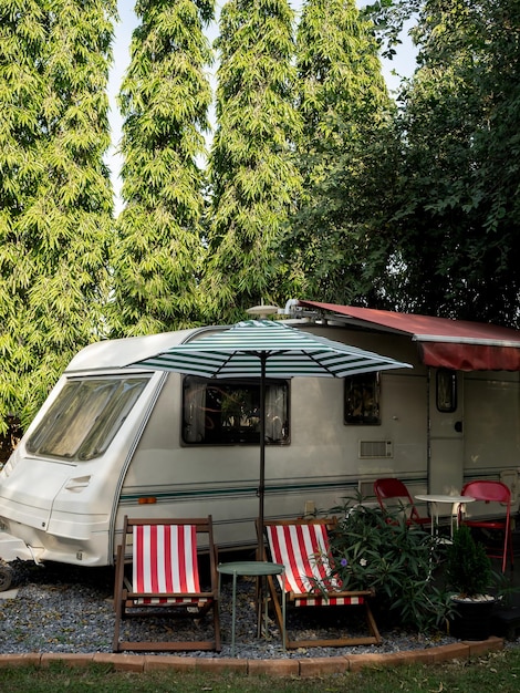 Oldtimer-Caravan-Parkplatz in Gartendekoration mit leeren Sitzen und Tisch auf großem Baumhintergrund im vertikalen Stil Entspannen Sie beim Camping und schlafen Sie im Wohnmobil-Anhänger Familienurlaub Reisekonzept