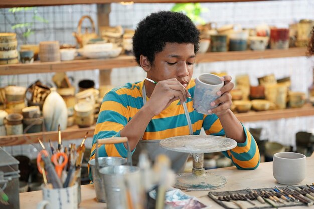 Oleiro de mão jovem afro fazendo vaso de barro na oficina de cerâmica, empresário.