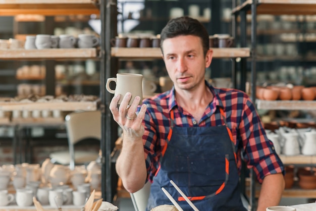 Oleiro masculino, olhando para o boné artesanal durante o dia de trabalho na cerâmica.