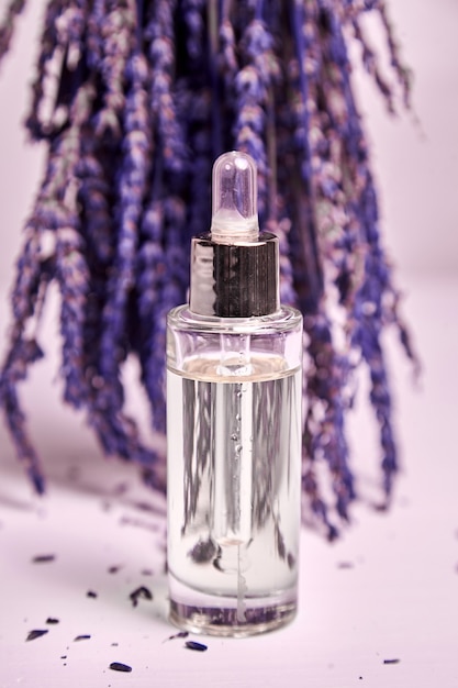 Óleo cosmético de lavanda em um frasco conta-gotas com pepit de vidro e flores secas de lavanda na mesa de madeira