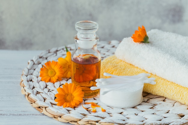 Óleo cosmético natural, tintura ou infusão, almofada de algodão, bastões e toalhas com flores de calêndula em cinza