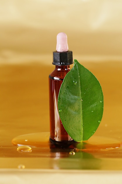 óleo de jojoba em garrafa marrom e folhas verdes em uma superfície de ouro