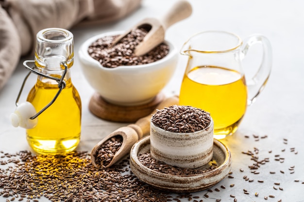 Óleo de linhaça em uma garrafa e tigela de cerâmica com sementes de linhaça marrons e colher de pau em um branco