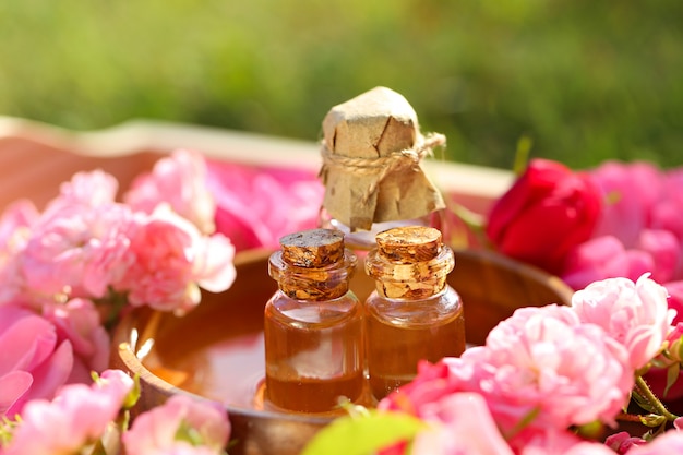 óleo de rosa. Spa conjunto óleo de pétalas de rosa, água de rosas em frasco de vidro. óleo de rosa natural em garrafas de vidro e rosas em uma bandeja de madeira. Conceito de massagem, aromaterapia e cosméticos orgânicos