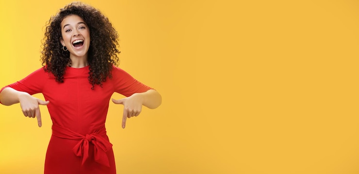 Foto olha o que eu tenho aqui, carismática, despreocupada, feliz e charmosa mulher com cabelo encaracolado em vestido vermelho rindo