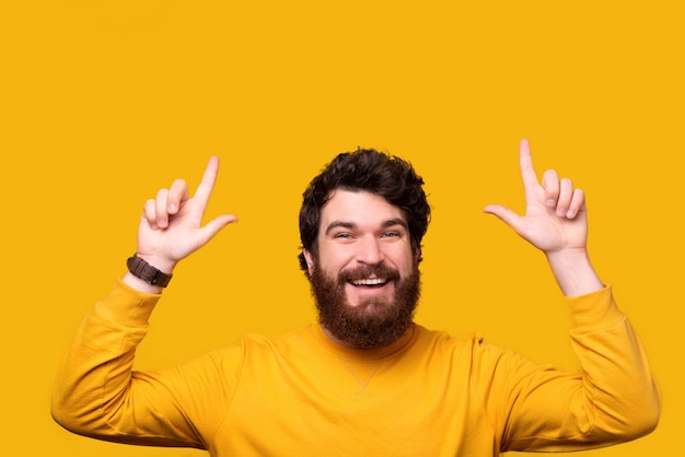 Olha, um homem barbudo está apontando para cima com as duas mãos em amarelo.