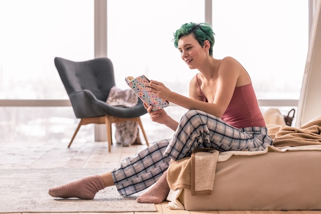 Olhando a programação. Jovem freelancer checando seu caderno, olhando a programação enquanto está sentado na cama