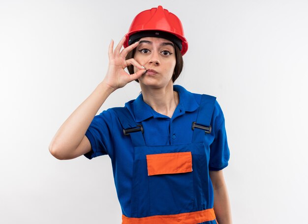 Olhando para a câmera, a jovem construtora de uniforme mostrando um gesto delicioso