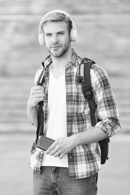 Olhar atraente vida escolar Ouvir música Jovem moderno e digital Homem na moda Estudante universitário Fones de ouvido smartphone Educação online Conceito de livro de áudio Tecnologia educacional e aprendizagem