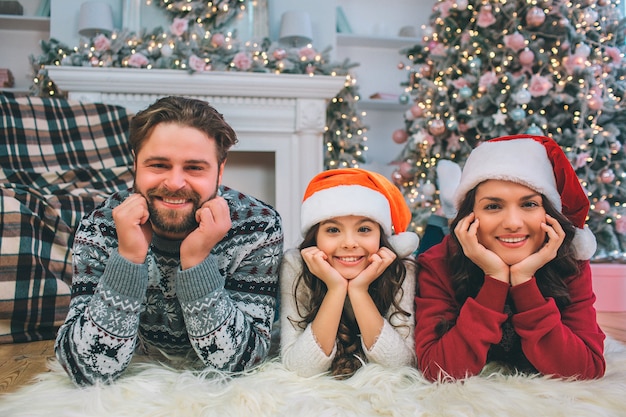 Olhar de família. Jovem, mulher e filha, deitado no chão e olhar. Eles posam. as pessoas dão as mãos sob o queixo. Eles sorriem.