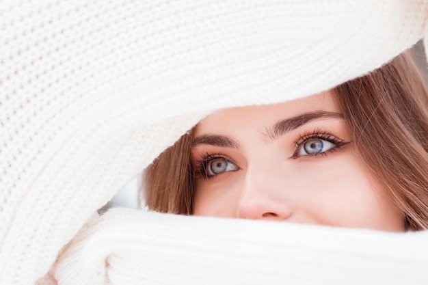 Olhar expressivo de olhos de mulher bonita através de mangas de suéter de malha branca, temporada de inverno.