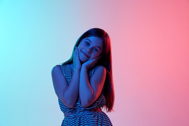 Olhar fofo, menina linda, posando sobre fundo de estúdio rosa azul gradiente em neon