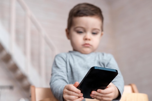 Olhar menino bonito da criança brincando com smartphone bebê saudável tocando o telefone móvel com os dedos ...