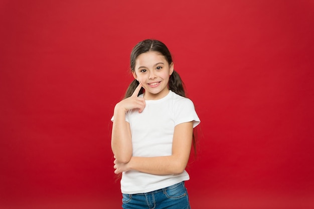 Olhar pensativo do modelo de cuidados com a pele Menina pequena mantendo o dedo na pele da bochecha Menina adorável sem maquiagem Cosméticos de beleza para crianças O cuidado perfeito com o rosto e a pele Ela é fofa