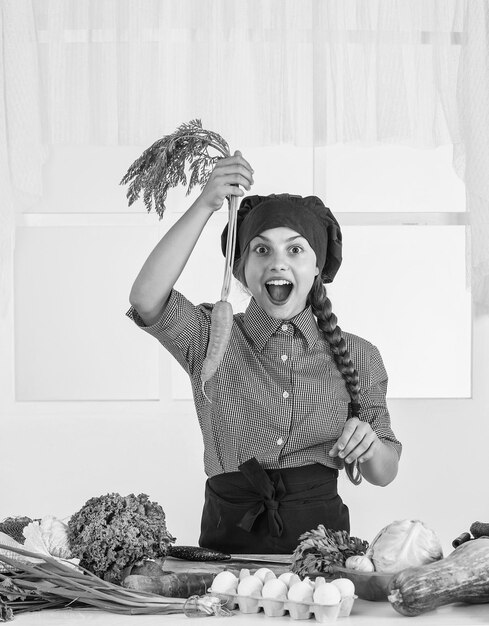 Olhe para aquele garoto vestindo uniforme de chef e chapéu adolescente preparando cenoura, legumes crus frescos, hora de comer criança feliz cozinhando na cozinha alimentos saudáveis e orgânicos apenas cheios de vitaminas