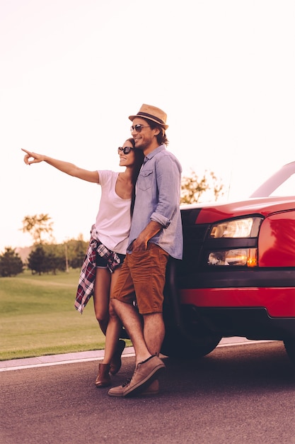 Foto olhe para isso! comprimento total de um lindo casal jovem se unindo e se inclinando em sua caminhonete enquanto uma mulher apontando para longe e sorrindo