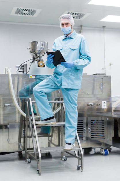 Olhe para o cientista da câmera em traje de laboratório em pequena escada de aço com tablet