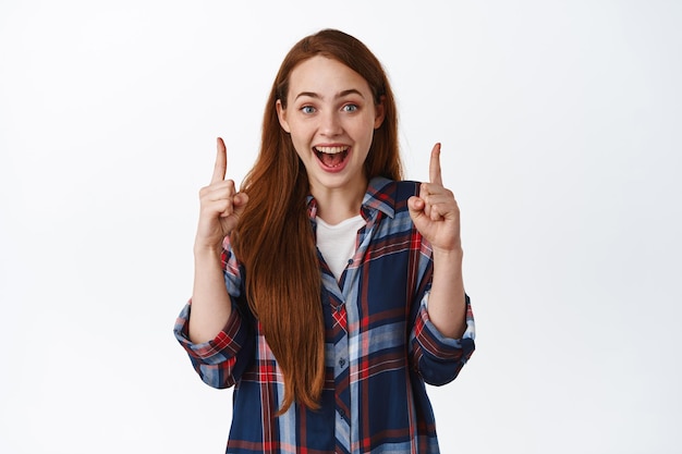 Olho para cima. Garota ruiva animada grita e aponta para o logotipo fantástico, mostrando propaganda promocional no topo, sorrindo amazd, de pé contra um fundo branco