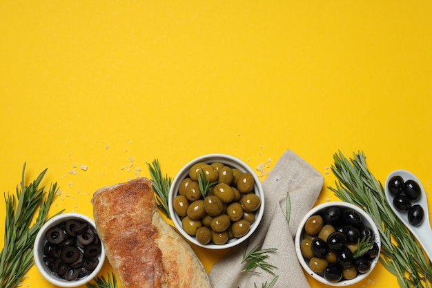 Oliven in Schalen, Rosmarin und Baguette auf gelbem Hintergrund, Platz für Text