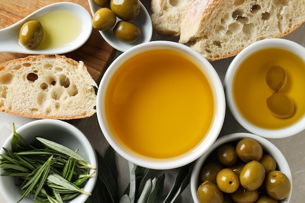 Olivenöl und Oliven in Schüsseln und Brotscheiben auf hellem Hintergrund von oben