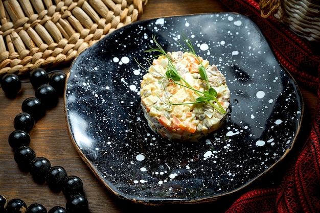Olivier-Salat mit Hühnergurken und Mayonnaise in einem Teller auf Holzhintergrund
