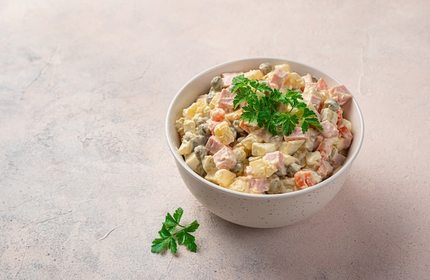 Oliviersalat mit Gemüse, Wurst und Mayonnaise auf hellem Hintergrund. Traditioneller russischer Salat.