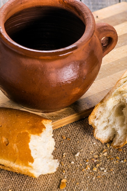 Olla de barro con leche y baguette en mesa de madera